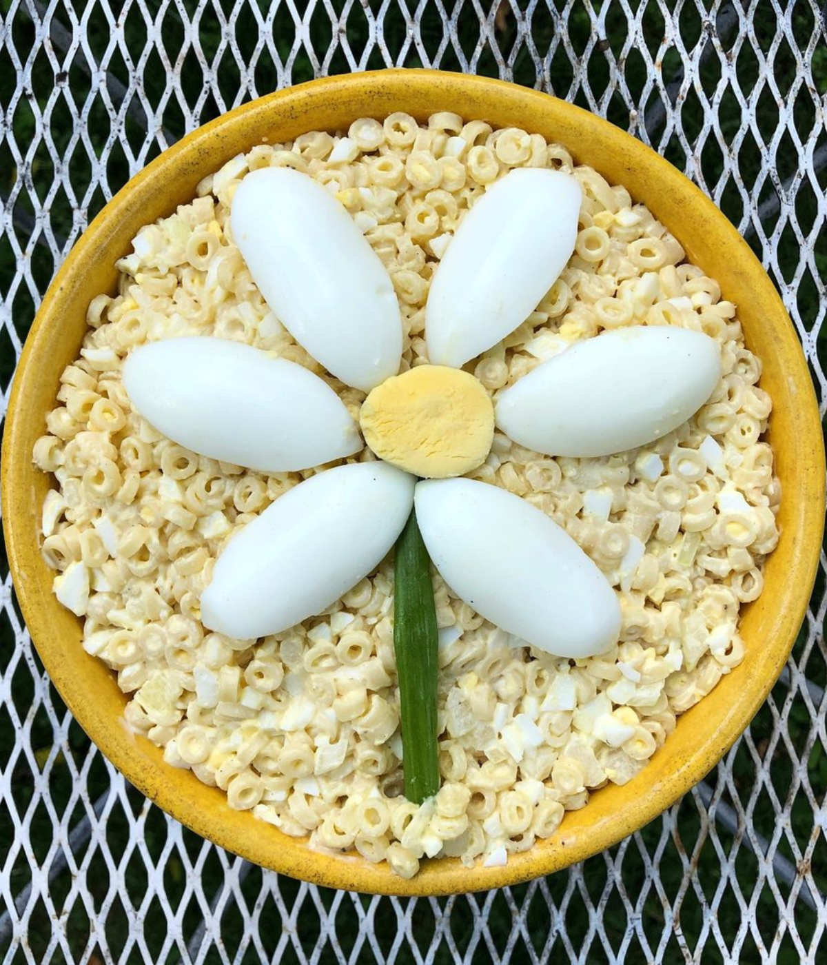 a yellow bowl with ring mac salad and a flower made of sliced eggs