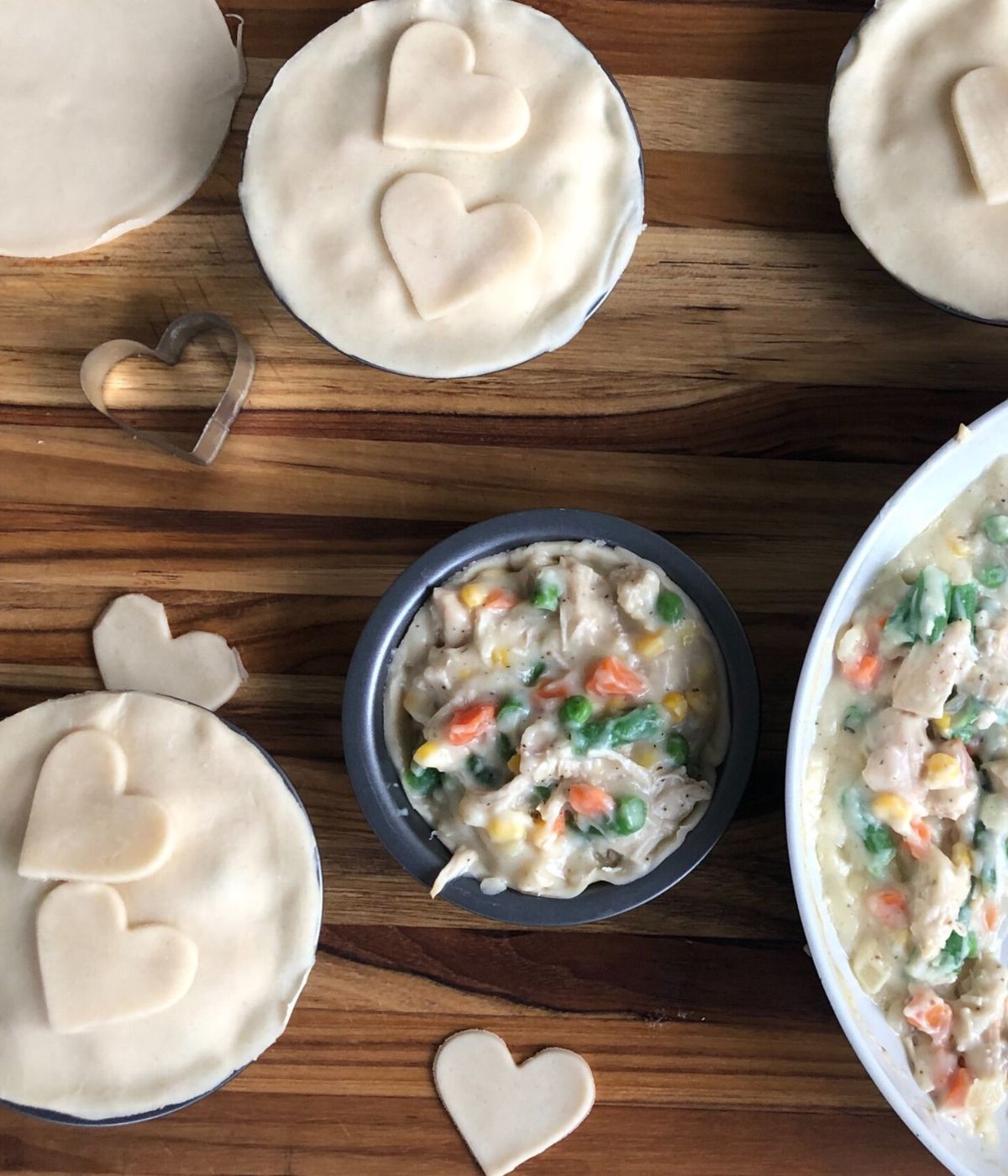 Chicken pot pie filling in a bowl surrounded by pot pie crusts with heart shaped crust cut-outs on top