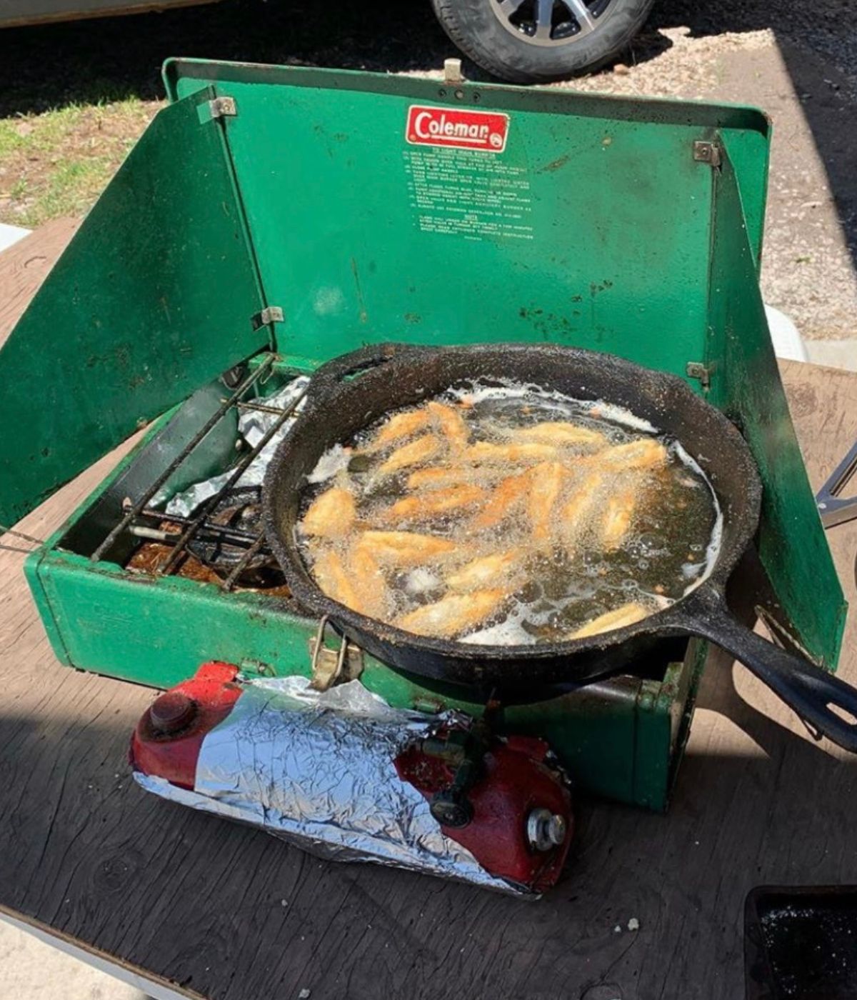 Breaded walleye cooking in a pan on a portable green stovetop